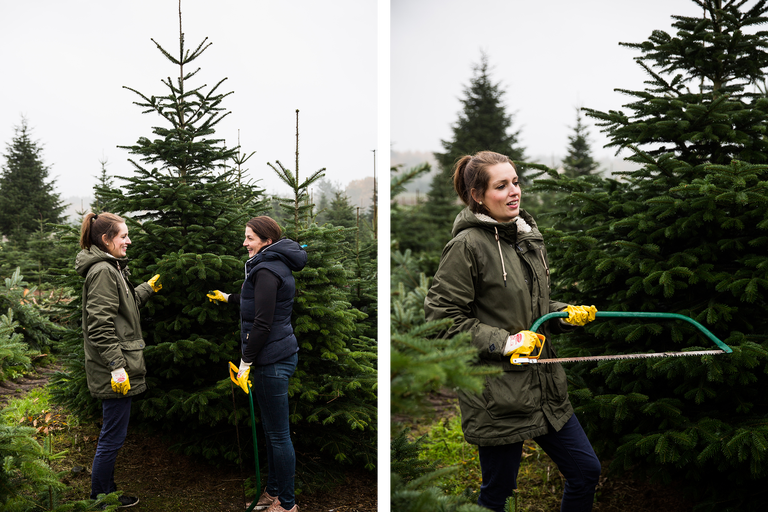 Zwei Frauen wählen im Freien einen Weihnachtsbaum aus, eine hält eine Baumsäge.