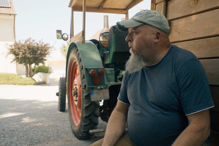 Mann sitzt neben einem Oldtimer Traktor