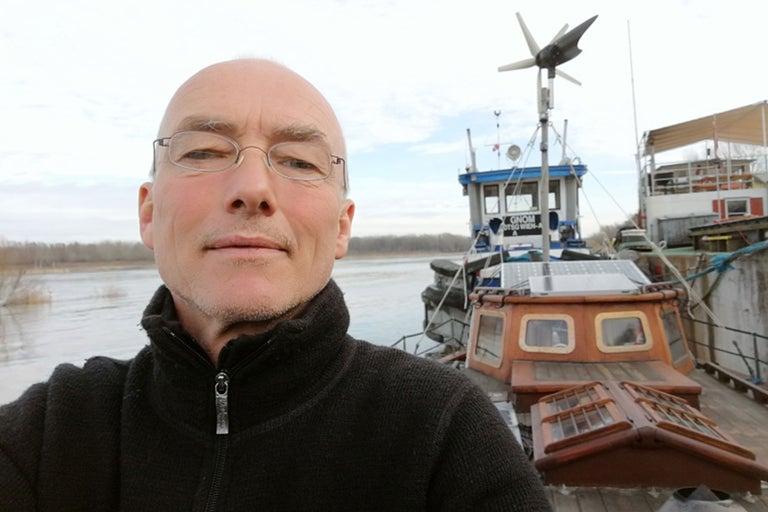 Mann vor einem Hausboot mit Solarpanelen und Windrad