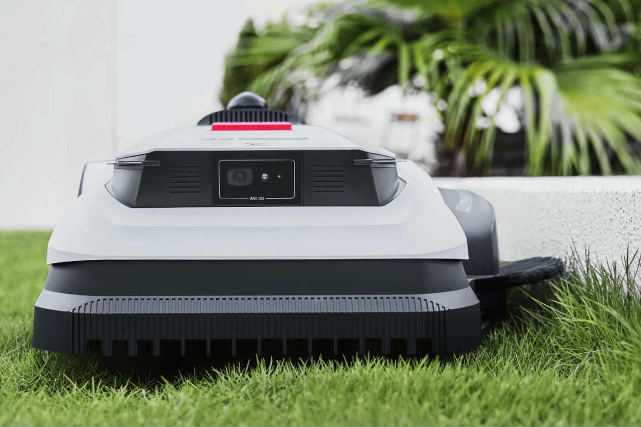 Mähroboter mit AIVI 3D Kamera auf einer Rasenfläche vor Pflanzen.