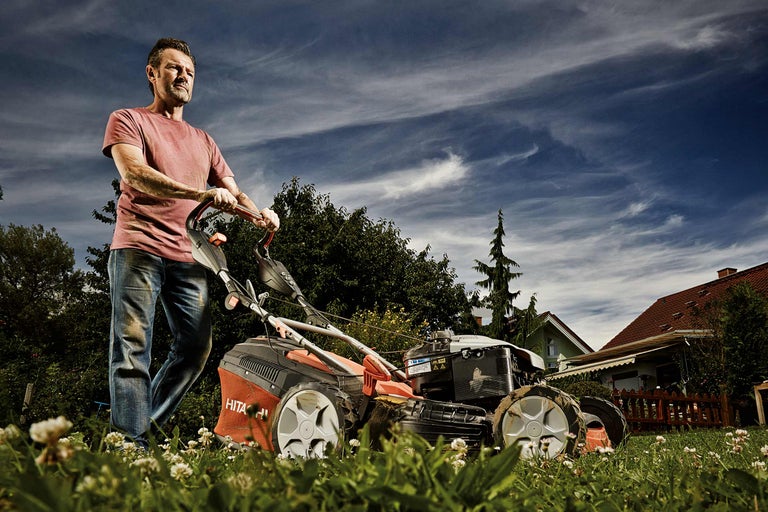 Mann mäht Rasen mit einem Rasenmäher im Garten.