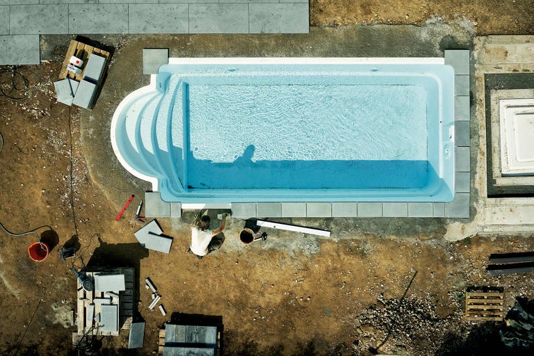 Aufbauszene eines Schwimmbeckens mit Wasser und umliegenden Pflastersteinen von oben.