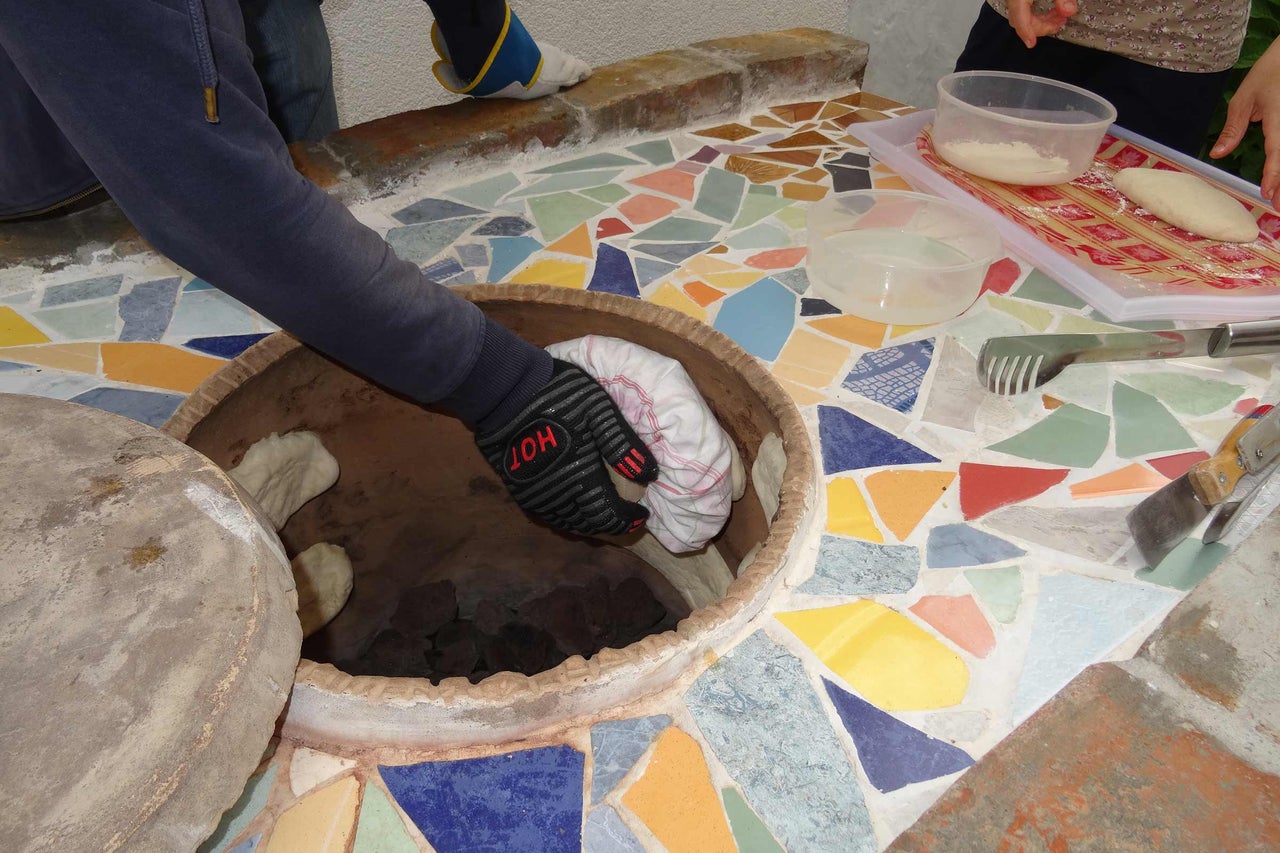 Brotbackofen mit Mosaikfliesen und Person, die Brot hineinlegt