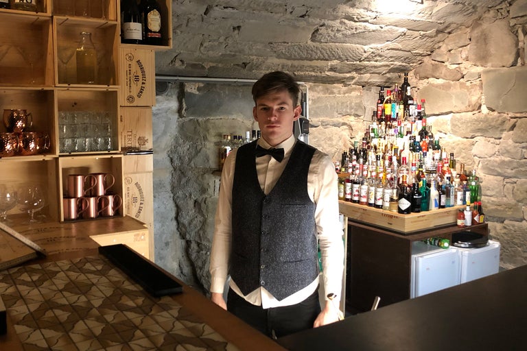 Innenaufnahme einer Bar mit einem Barkeeper, dekoriert mit Getränkeflaschen, Holzkisten und Barzubehör
