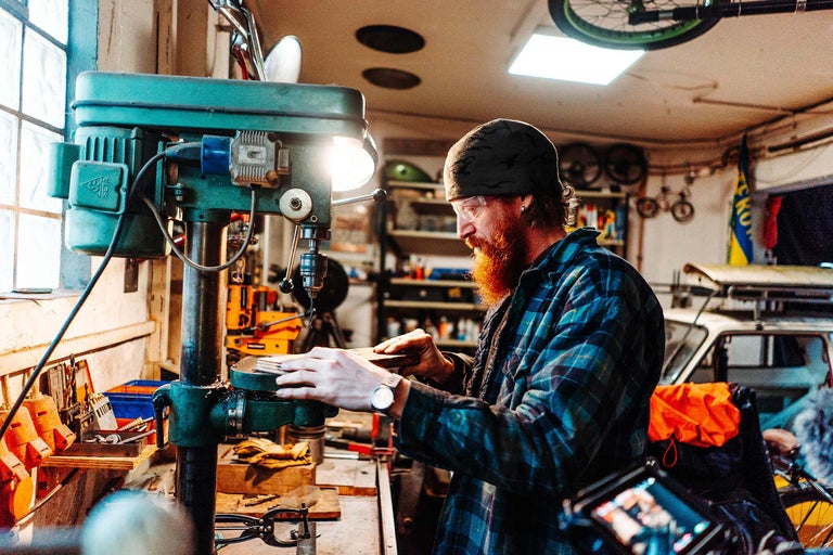 Werkstatt mit einer stehenden Bohrmaschine in der ein Mann ein Werkstück bearbeitet.