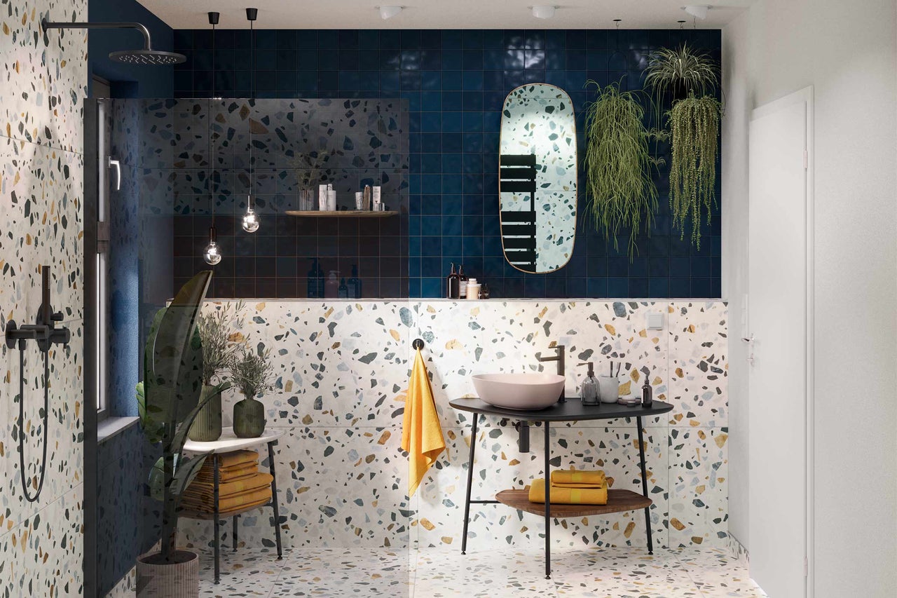 Helles Badezimmer mit Terrazzoboden, Waschbecken auf einem Waschtisch mit Handtüchern, Dusche und blauen Fliesen