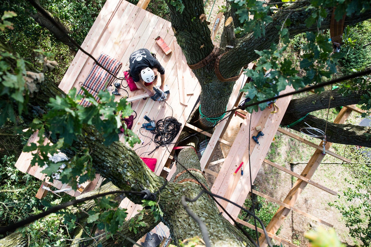 Baumhausbau mit einer Person auf einer Holzplattform in den Baumwipfeln.