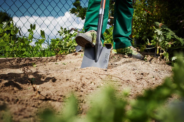 Gartenszene mit Person, die einen Spaten in den Boden drückt.