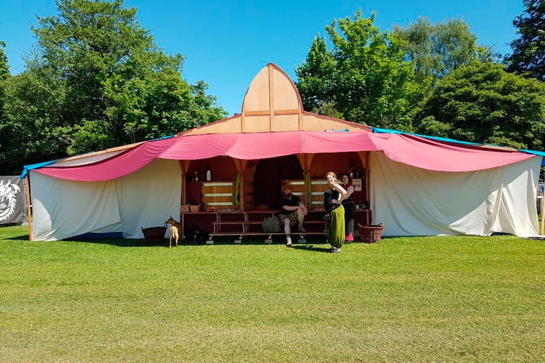 Szene mit einem Holzpavillon mit Textilbespannung auf einer Rasenfläche.