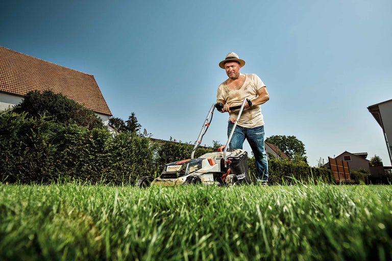 Mann mäht Rasen mit einem Rasenmäher der Marke Pattfield in seinem Garten.
