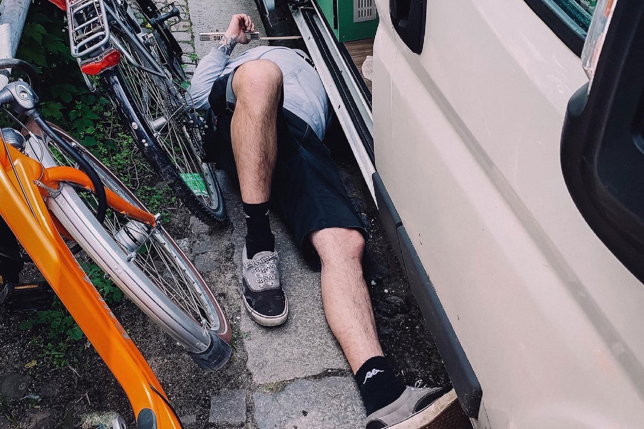 Eine Person liegt unter einem Fahrzeug, neben Fahrrädern.
