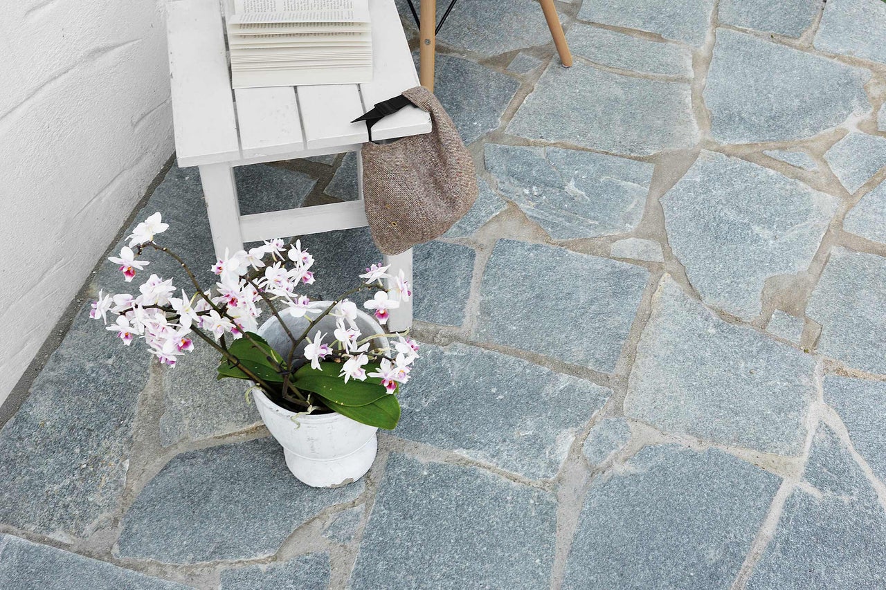 Terrasse mit Natursteinplatten, dekoriert mit Tisch, Büchern, Tasche und Topfpflanze