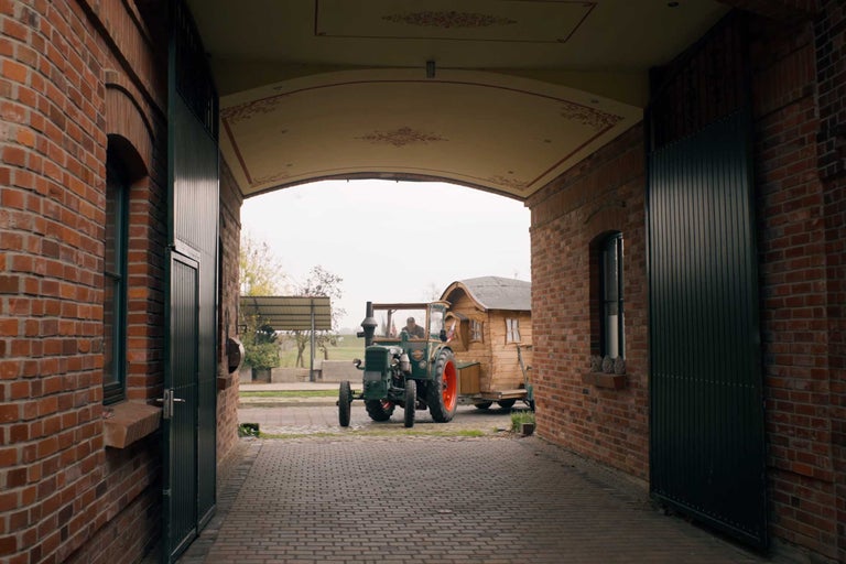 Blick durch eine Toröffnung auf einen Traktor mit Anhänger vor einem Bauernhaus