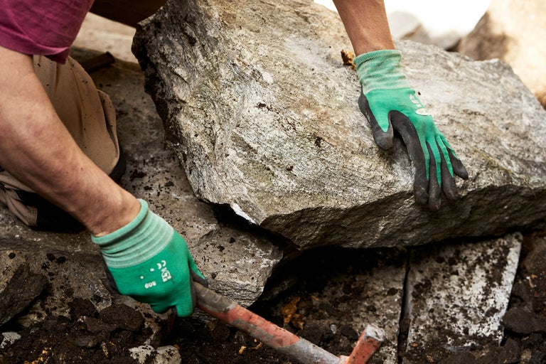 Person setzt einen großen Stein mit einem Werkzeug und Handschuhen.