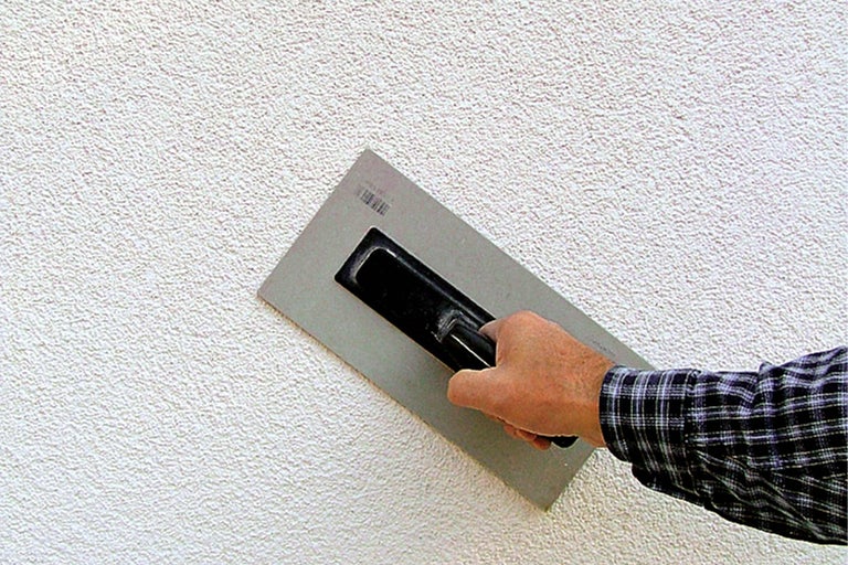 Außenwand mit Putzstruktur und Handwerker mit Glättkelle