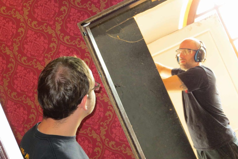 Zwei Männer montieren eine Tür. Der eine trägt einen Gehörschutz und eine Schutzbrille.