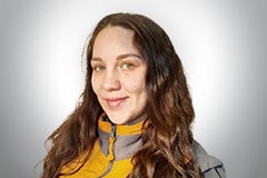 Porträt einer lächelnden Frau mit langen, gewellten Haaren.