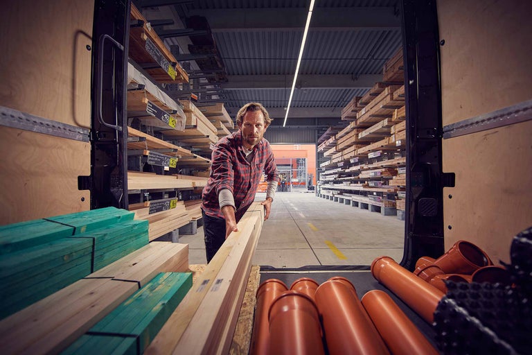 Ein Mann lädt Holzlatten und Rohre in einen Transporter im Hornbach Baumarkt.