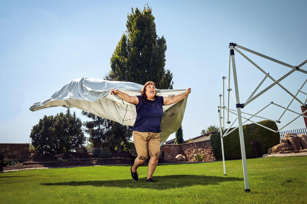 Frau, die eine Pavillonplane im Garten ausbreitet, umgeben von Bäumen und einem Pavillongestell