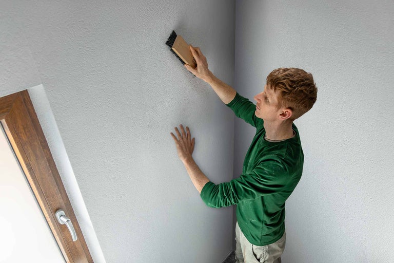 Mann strukturiert Wand mit Bürste