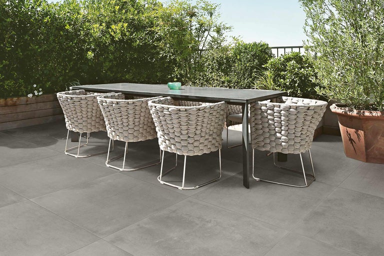 Esstisch mit Korbstühlen auf grauen Terrassenplatten im Garten