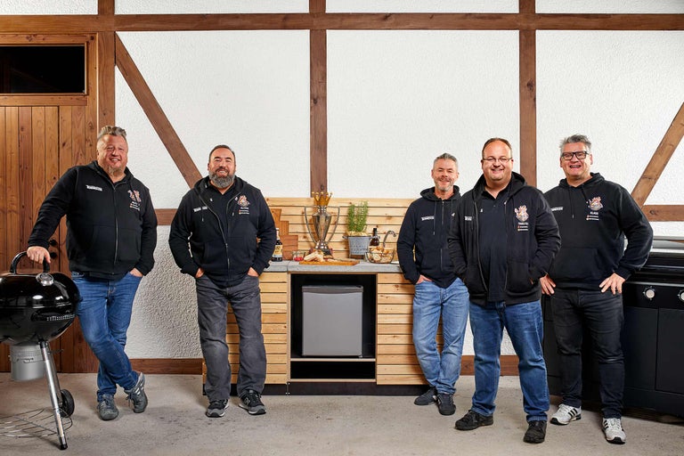 Fünf Männer vor einer Holzküche mit Grill und Kühlschrank