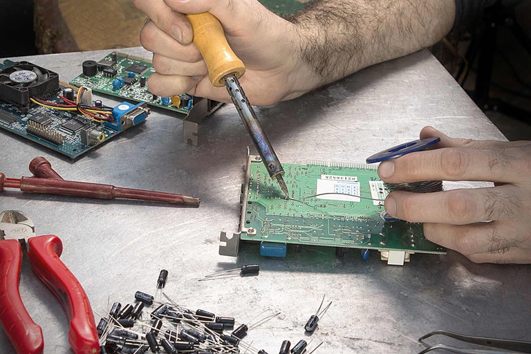 Löten einer elektronischen Platine mit Lötkolben und Lötzinn auf einem Werkstatttisch.