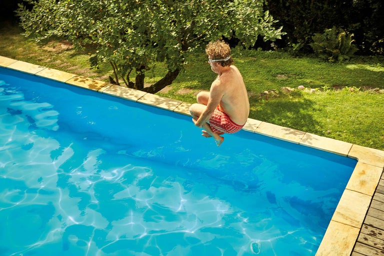 Mann springt in Schwimmbecken im Garten.