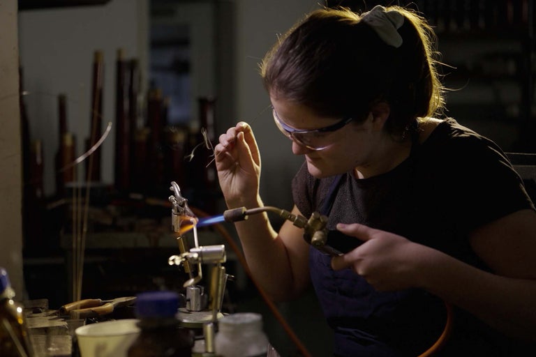 Frau mit Schutzbrille und Lötlampe bei der Glasbearbeitung.