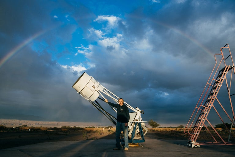 Ein Mann steht neben einem Teleskop unter einem Regenbogen