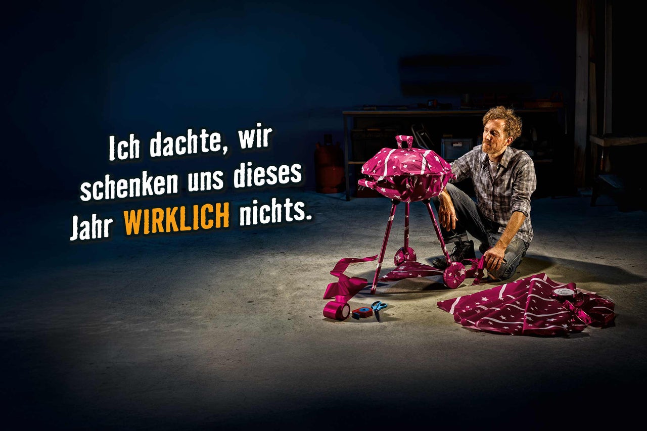 Ein verpackter Kugelgrill als Geschenk mit einer Person im Hintergrund.