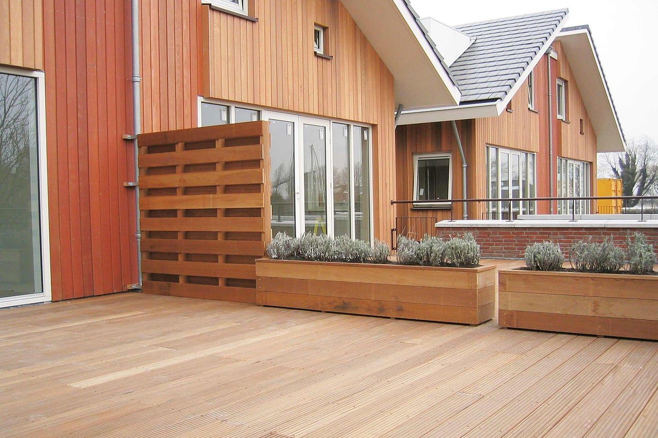 Holzterrasse mit Sichtschutz und bepflanzten Blumenkästen vor einem Haus
