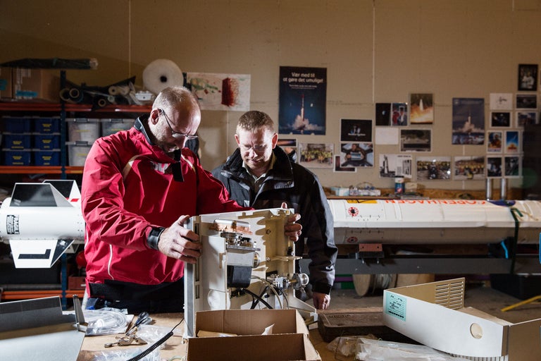 Zwei Personen arbeiten an einer Rakete in einer Werkstatt.
