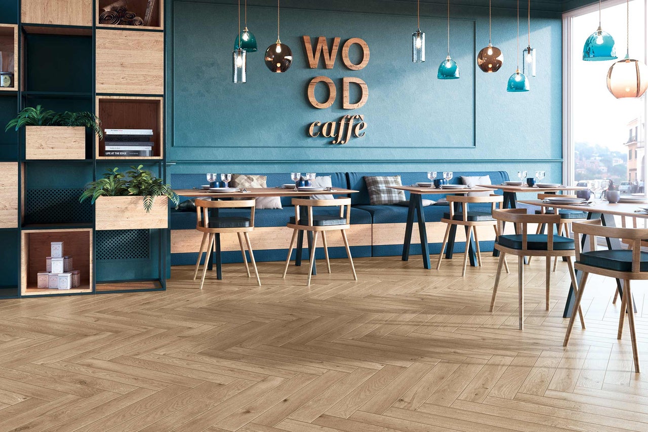 Innenaufnahme eines Cafés mit Tischen, Stühlen und Holzfußboden im Fischgrätmuster.