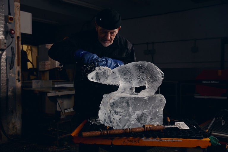 Ein Mann formt eine Eisbär-Skulptur aus Eisblöcken mit Werkzeugen.