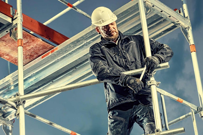 Ein Mann mit Schutzhelm montiert ein Gerüst.