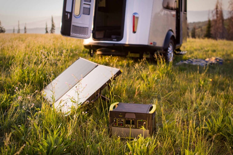 Solarpanel und Powerstation im Gras vor einem Wohnwagen
