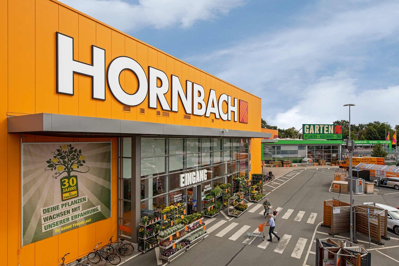  Außenansicht einer Hornbach Filiale mit Eingang, Pflanzen und Parkplatz 