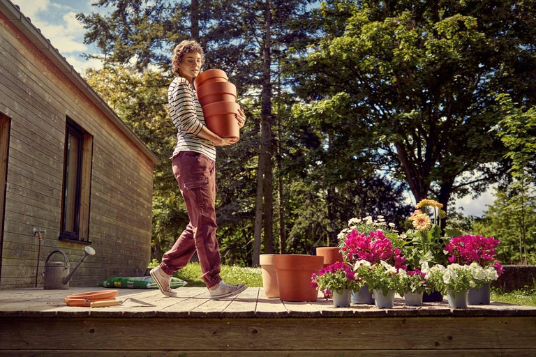 Frau trägt Pflanzgefäße im Garten auf einer Holzterrasse