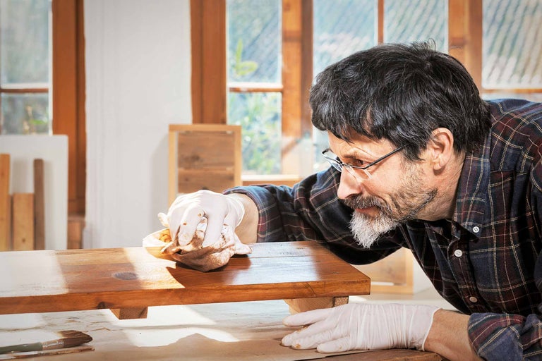 Mann trägt Holzlasur mit Lappen auf Werkstück auf