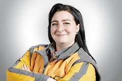 Eine lächelnde Frau mit verschränkten Armen in Arbeitskleidung