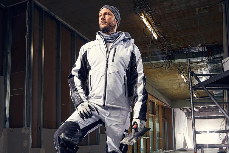 Handwerker in Arbeitskleidung mit Maurerkelle auf einer Baustelle.