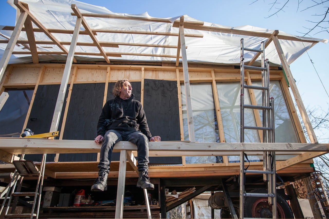 Mann sitzt auf Holzkonstruktion eines Hauses im Bau
