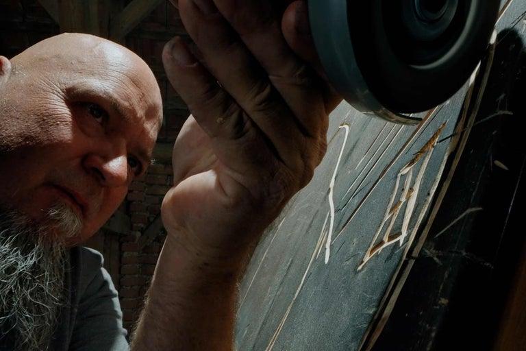 Mann arbeitet mit einem Winkelschleifer an einem Werkstück aus Holz.