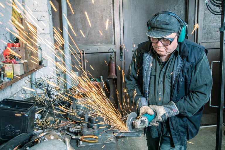 Ein Mann arbeitet mit einer Flex in einer Werkstatt, wobei Funken sprühen. Er trägt Schutzkleidung.