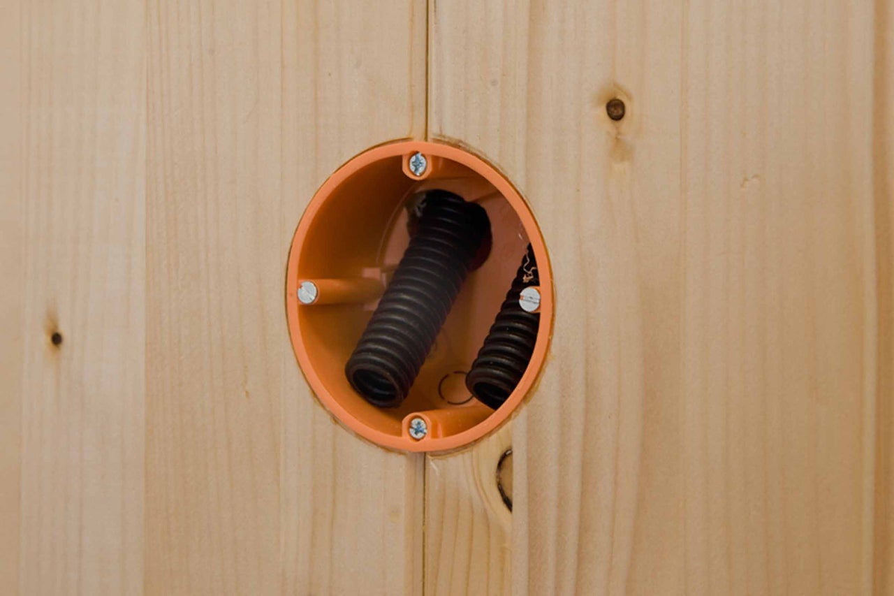 Hohlwanddose montiert in einer Holzverkleidung mit zwei schwarzen Wellrohren für die Elektroinstallation.