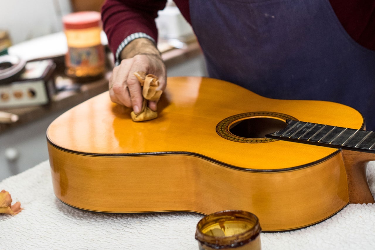 Eine Person poliert eine Gitarre mit einem Tuch. Gitarrenpflege.