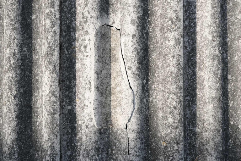 Nahaufnahme einer beschädigten, gewellten Faserzementplatte mit Riss.