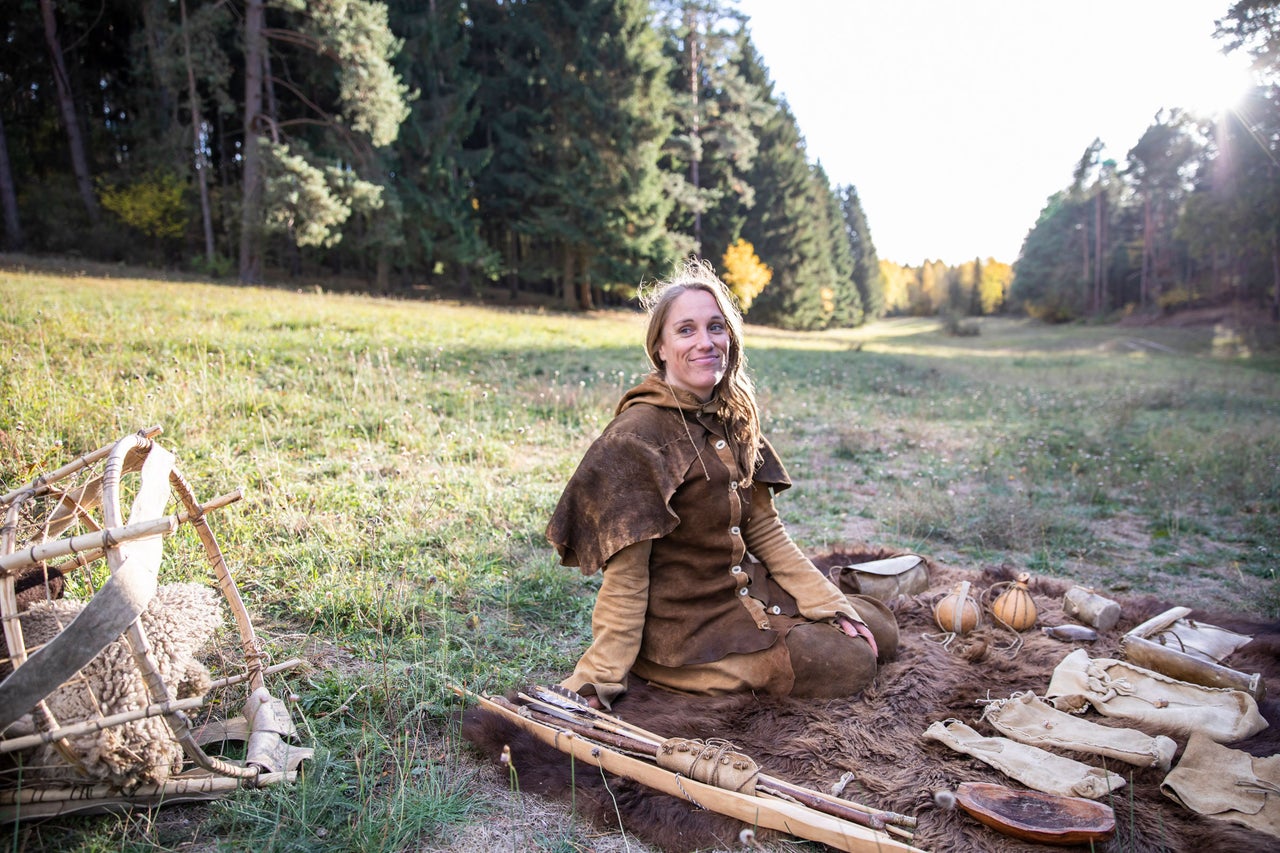 Frau in historischer Kleidung sitzt auf einer Wiese mit historischer Ausrüstung.