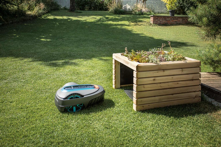 Szene im Garten mit Rasenroboter und Pflanztisch aus Holz.